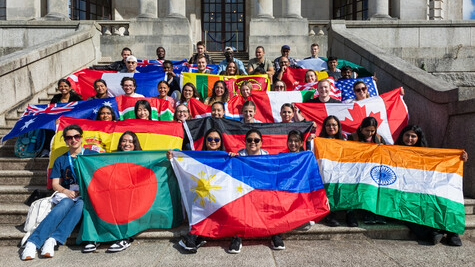 A group of international students sitting on steps with representing flags.