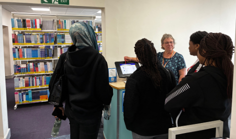 Group of students surrounding a computer with a librarian offering support