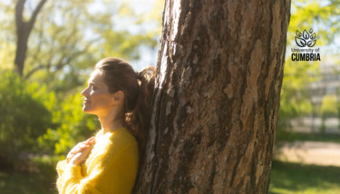 A student standing with their back against a tree in nature. 