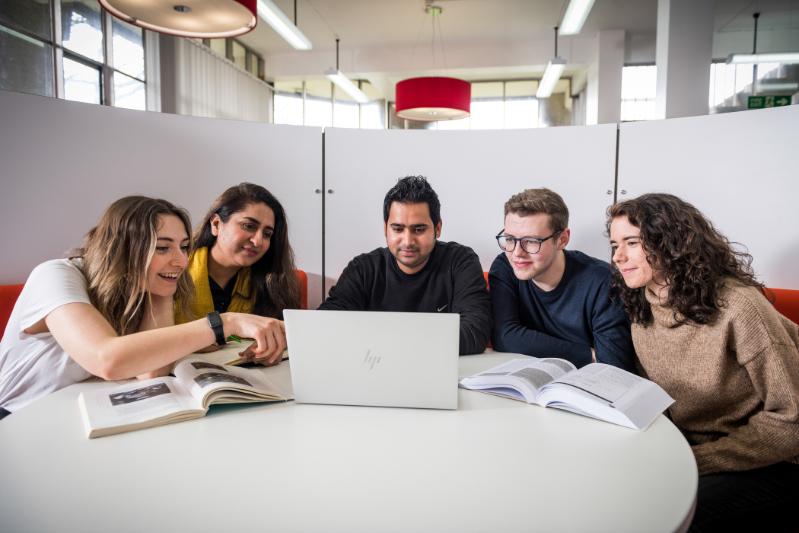 Group of students sat at a desk, looking at a laptop