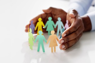 A pair of hands crowding around a group of paper cut out people.