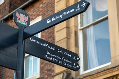 A street sign displaying a railway station and university campus