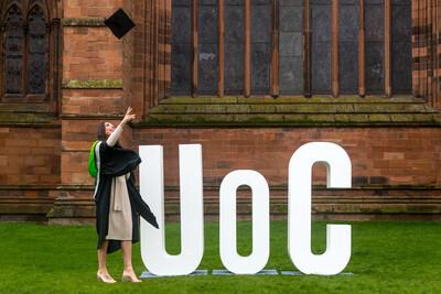 An image of a student throwing a cap in the air in front of the UOC letters.