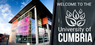 Modern University of Cumbria campus building with a glass-fronted facade illuminated in pink and purple tones, alongside a large sign displaying the University of Cumbria logo and name. Blue sky and surrounding campus environment visible, showcasing a contemporary UK higher education institution.