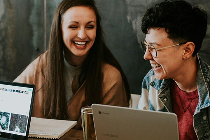 Two university students laughing and collaborating on a laptop during a study session.