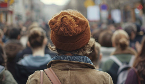 A medium close-up of a person standing up in a crowd to speak the truth, with others around them sitting quietly