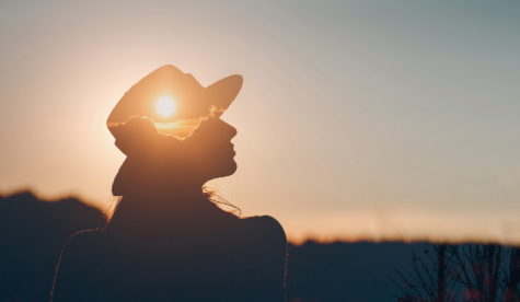 An adult silhouette sitting in a sunrise.