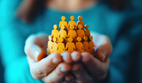 Hands holding a group of paper cut out figures.